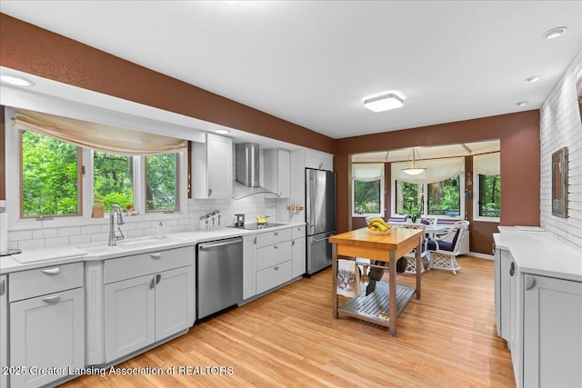 1122 Farwood Dr, East Lansing, MI 48823 - kitchen featuring appliances with stainless steel finishes, light countertops, backsplash, wall chimney exhaust hood, and light wood-style flooring