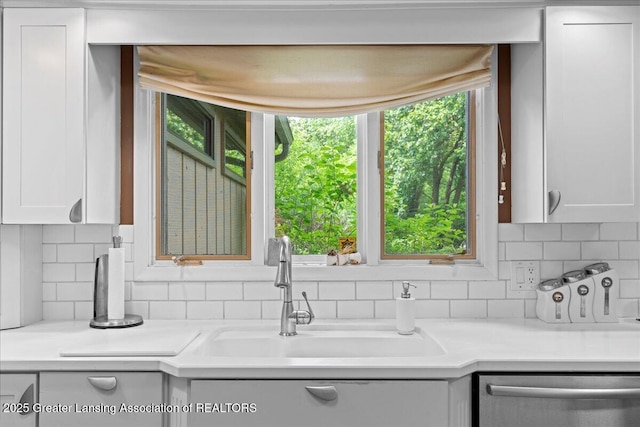 1122 Farwood Dr, East Lansing, MI 48823 - kitchen featuring stainless steel dishwasher, tasteful backsplash, light countertops, and white cabinetry