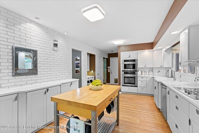 1122 Farwood Dr, East Lansing, MI 48823 - kitchen with appliances with stainless steel finishes, light countertops, backsplash, light wood-type flooring, and brick wall