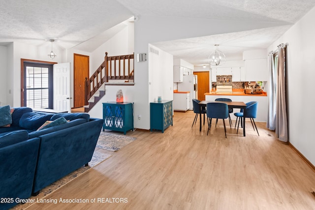 2440 Sower Blvd, Okemos, MI 48864 - living area with lofted ceiling, light wood-style floors, a chandelier, stairway, and a textured ceiling