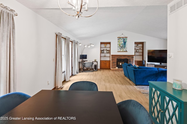 2440 Sower Blvd, Okemos, MI 48864 - dining area featuring light wood finished floors, vaulted ceiling, a chandelier, built in features, and a fireplace