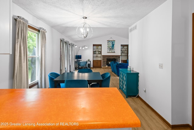 2440 Sower Blvd, Okemos, MI 48864 - dining space featuring light wood finished floors, lofted ceiling, a chandelier, a textured ceiling, and a fireplace