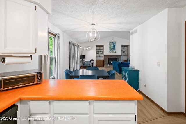2440 Sower Blvd, Okemos, MI 48864 - kitchen with a peninsula, light wood-style flooring, a textured ceiling, white cabinetry, and lofted ceiling