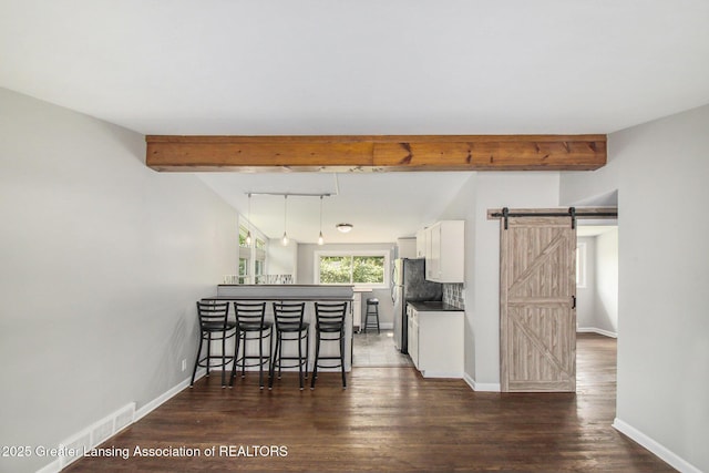 1321 Weber Dr, Lansing, MI 48912 - kitchen featuring a barn door, beam ceiling, white cabinetry, dark wood-style flooring, and a kitchen breakfast bar