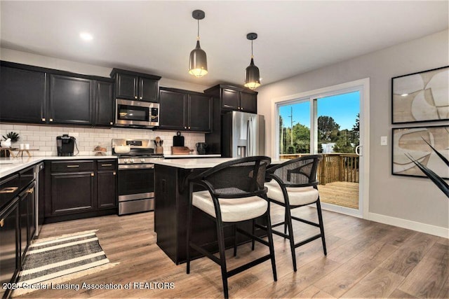 2905 Moccasin Dr, Dewitt, MI 48820 - kitchen with stainless steel appliances, dark cabinetry, a kitchen bar, and decorative backsplash