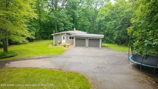 9481 S Clinton Trl, Eaton Rapids, MI 48827 - garage featuring a trampoline, asphalt driveway, and a view of trees