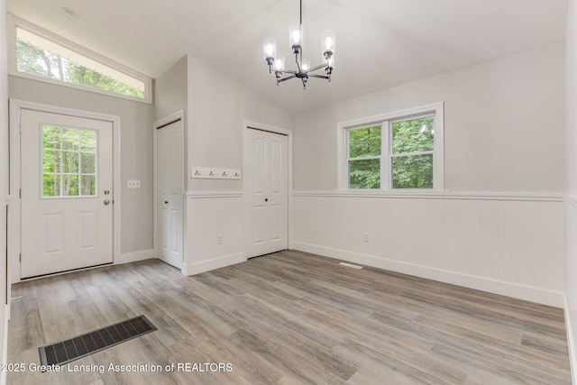9481 S Clinton Trl, Eaton Rapids, MI 48827 - foyer with a chandelier, plenty of natural light, vaulted ceiling, light wood-style floors, and a wainscoted wall