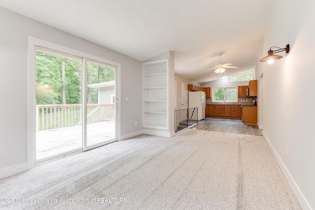 9481 S Clinton Trl, Eaton Rapids, MI 48827 - unfurnished living room featuring vaulted ceiling, light carpet, ceiling fan, and built in shelves