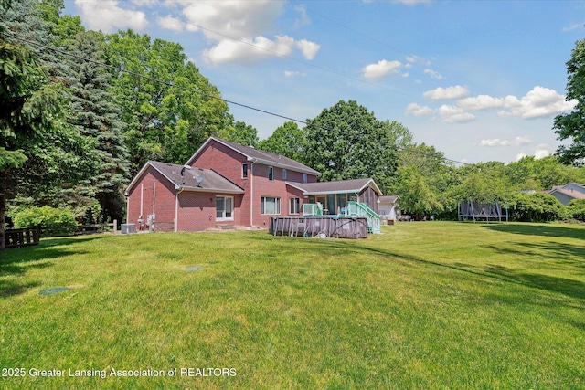 4084 Hulett Rd, Okemos, MI 48864 - rear view of house featuring a trampoline, brick siding, a lawn, and a wooden deck