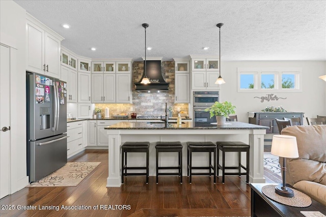 11167 Windswept Dr, Grand Ledge, MI 48837 - kitchen with appliances with stainless steel finishes, wall chimney exhaust hood, dark wood-style floors, a breakfast bar, and tasteful backsplash