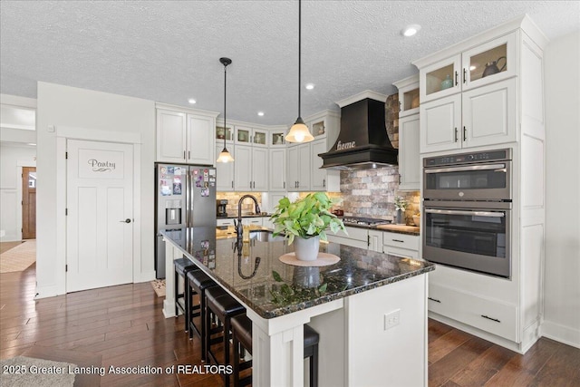 11167 Windswept Dr, Grand Ledge, MI 48837 - kitchen featuring custom range hood, stainless steel appliances, dark wood-style floors, tasteful backsplash, and glass insert cabinets