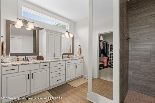 11167 Windswept Dr, Grand Ledge, MI 48837 - full bathroom featuring double vanity, a spacious closet, wood finished floors, and tiled shower