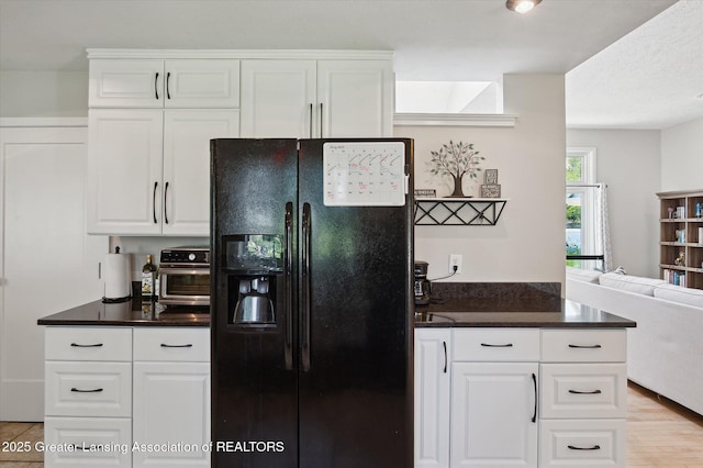 2605 College Rd, Holt, MI 48842 - kitchen with black fridge with ice dispenser, dark countertops, open floor plan, and white cabinets
