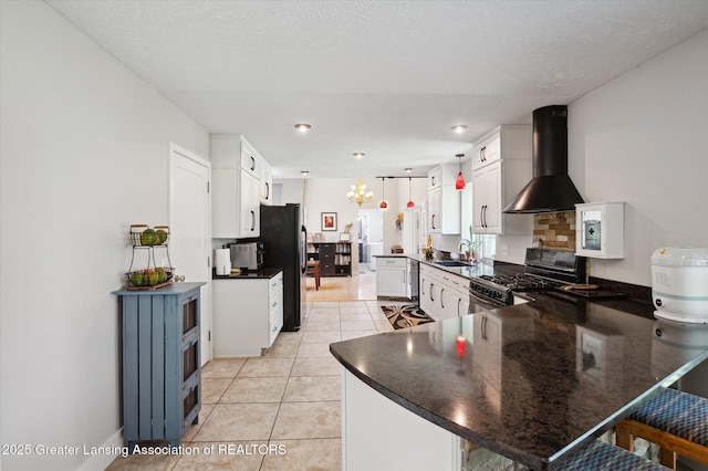 2605 College Rd, Holt, MI 48842 - kitchen with wall chimney range hood, stainless steel gas range, freestanding refrigerator, dark countertops, and a peninsula