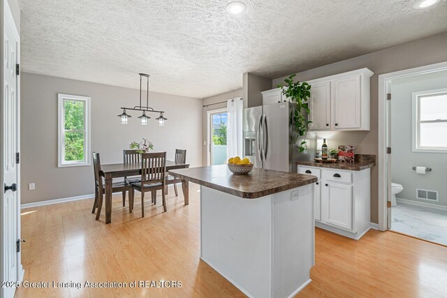 774 Tims View St, Potterville, MI 48876 - kitchen featuring stainless steel refrigerator with ice dispenser, dark countertops, light wood-type flooring, white cabinets, and a textured ceiling