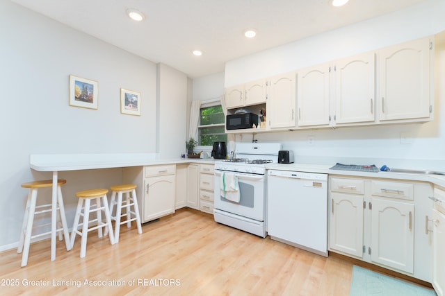 2162 Kent St, Okemos, MI 48864 - kitchen featuring white appliances, recessed lighting, light countertops, light wood-style floors, and a kitchen bar