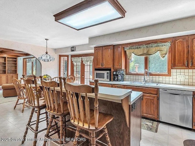 3619 W Arbutus Dr, Okemos, MI 48864 - kitchen featuring stainless steel appliances, arched walkways, a breakfast bar area, brown cabinets, and a center island
