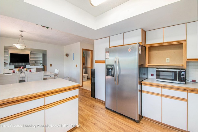 12829 Silver Ridge Dr, Grand Ledge, MI 48837 - kitchen with stainless steel appliances, light wood finished floors, white cabinets, light countertops, and decorative backsplash