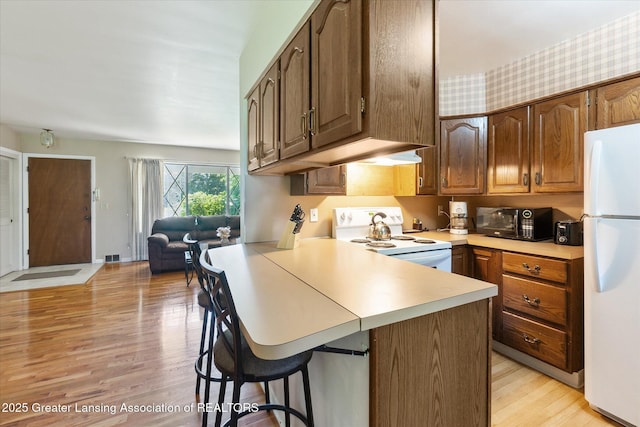 1117-1119 Blake Ave, Lansing, MI 48912 - kitchen featuring white appliances, a kitchen bar, light countertops, light wood finished floors, and a peninsula