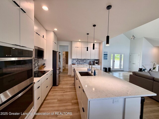 10993 Lakeside Dr, Perrinton, MI 48871 - kitchen featuring appliances with stainless steel finishes, modern cabinets, light wood-style flooring, decorative backsplash, and white cabinetry