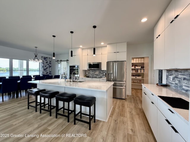 10993 Lakeside Dr, Perrinton, MI 48871 - kitchen featuring appliances with stainless steel finishes, modern cabinets, a kitchen bar, decorative backsplash, and light wood finished floors