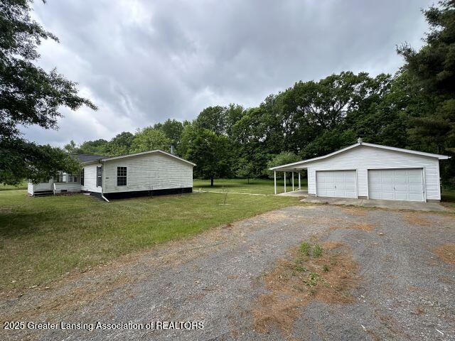 8241 Barson Rd, Rives Junction, MI 49277 - view of property exterior featuring a detached garage, an outbuilding, a lawn, and view of wooded area