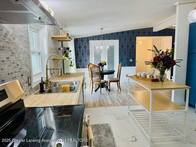 4340 Balmoral Dr, Lansing, MI 48911 - kitchen with stainless steel range with electric stovetop, exhaust hood, light marble finish flooring, a wainscoted wall, and a chandelier