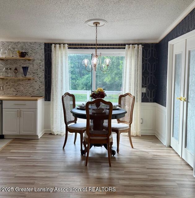 4340 Balmoral Dr, Lansing, MI 48911 - dining room featuring a textured ceiling, a chandelier, light wood-type flooring, a wainscoted wall, and ornamental molding