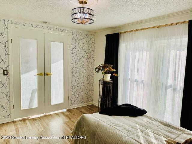 4340 Balmoral Dr, Lansing, MI 48911 - bedroom featuring wallpapered walls, french doors, wood finished floors, a textured ceiling, and a chandelier