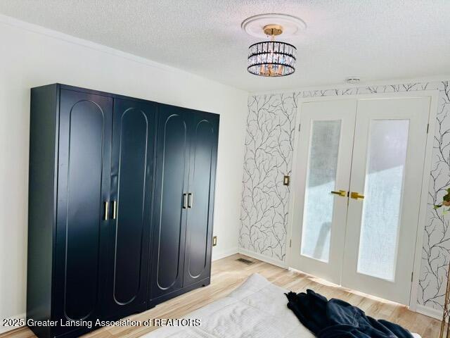 4340 Balmoral Dr, Lansing, MI 48911 - bedroom with french doors, light wood-type flooring, a textured ceiling, and a chandelier