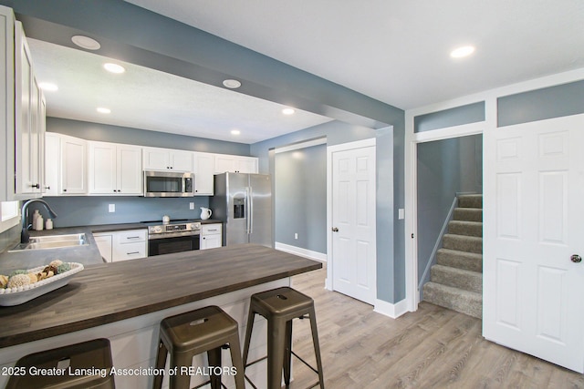 304 W Gibbs St, Saint Johns, MI 48879 - kitchen with stainless steel appliances, wood counters, light wood-style floors, a kitchen breakfast bar, and white cabinets
