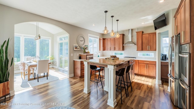 9655 Tobermory Dr, Haslett, MI 48840 - kitchen with wall chimney range hood, brown cabinets, arched walkways, a kitchen bar, and wood finished floors