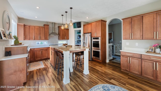 9655 Tobermory Dr, Haslett, MI 48840 - kitchen featuring appliances with stainless steel finishes, wall chimney exhaust hood, a breakfast bar area, brown cabinetry, and recessed lighting