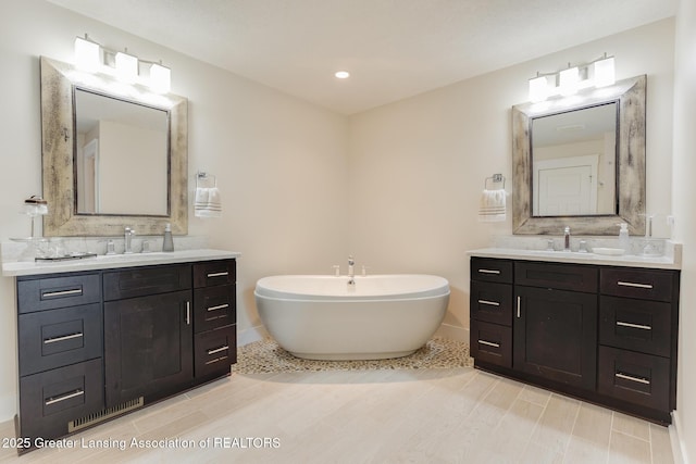 6075 Sacramento Way E, Lansing, MI 48823 - full bath featuring a freestanding tub, two vanities, wood finished floors, decorative backsplash, and recessed lighting