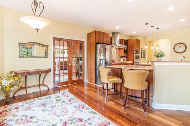 10696 W Clark Rd, Eagle, MI 48822 - kitchen with appliances with stainless steel finishes, wall chimney exhaust hood, brown cabinetry, wood finished floors, and french doors