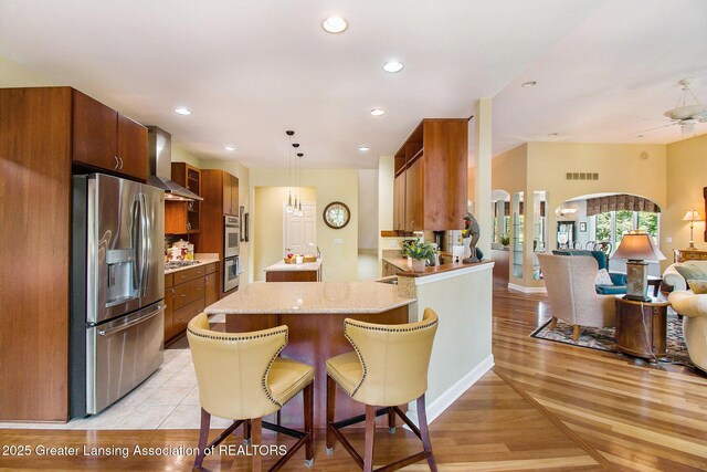 10696 W Clark Rd, Eagle, MI 48822 - kitchen with stainless steel appliances, wall chimney range hood, open floor plan, a peninsula, and hanging light fixtures