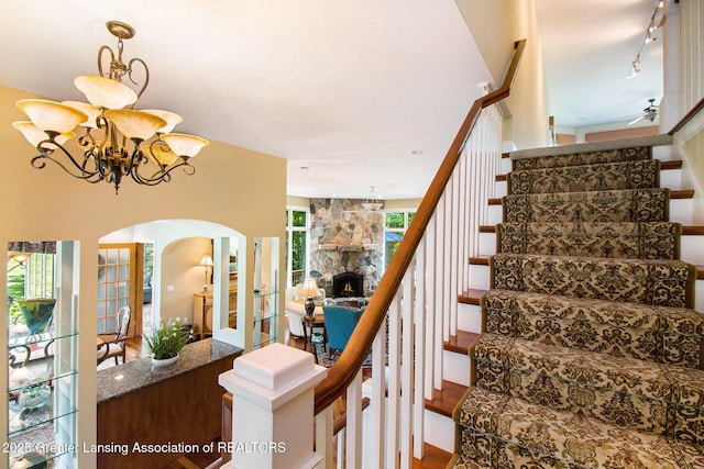 10696 W Clark Rd, Eagle, MI 48822 - stairs featuring arched walkways, track lighting, a chandelier, wood finished floors, and a stone fireplace