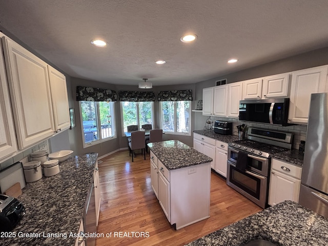 2665 Allium Dr, Holt, MI 48842 - kitchen featuring stainless steel appliances, light wood-style floors, white cabinets, a kitchen island, and decorative backsplash