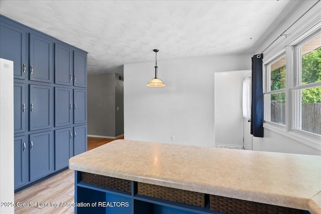 2218 Coolridge Rd, Holt, MI 48842 - kitchen featuring blue cabinets, light wood finished floors, hanging light fixtures, and light countertops