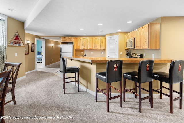 14747 Forest Hill Rd, Grand Ledge, MI 48837 - kitchen with stainless steel microwave, light carpet, freestanding refrigerator, a peninsula, and light countertops