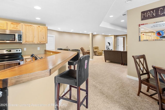 14747 Forest Hill Rd, Grand Ledge, MI 48837 - kitchen featuring stainless steel appliances, light brown cabinets, light carpet, recessed lighting, and a kitchen bar