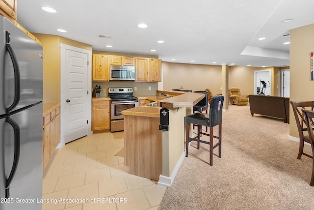 14747 Forest Hill Rd, Grand Ledge, MI 48837 - kitchen featuring appliances with stainless steel finishes, a kitchen breakfast bar, recessed lighting, light brown cabinets, and a peninsula