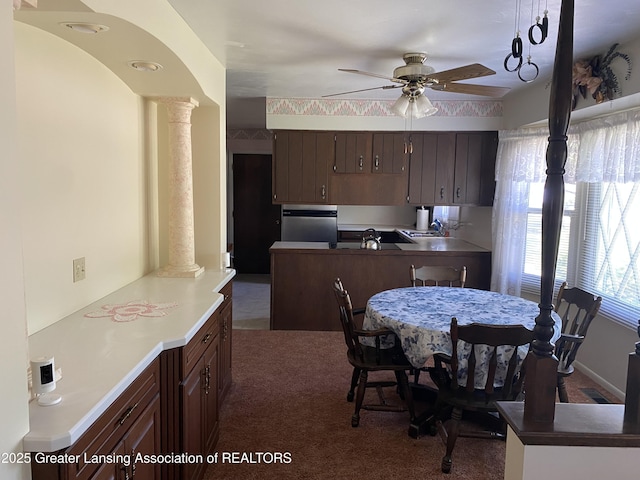 3931 Berry Ridge Dr, Holt, MI 48842 - kitchen with decorative columns, ceiling fan, dark carpet, dark brown cabinetry, and a peninsula
