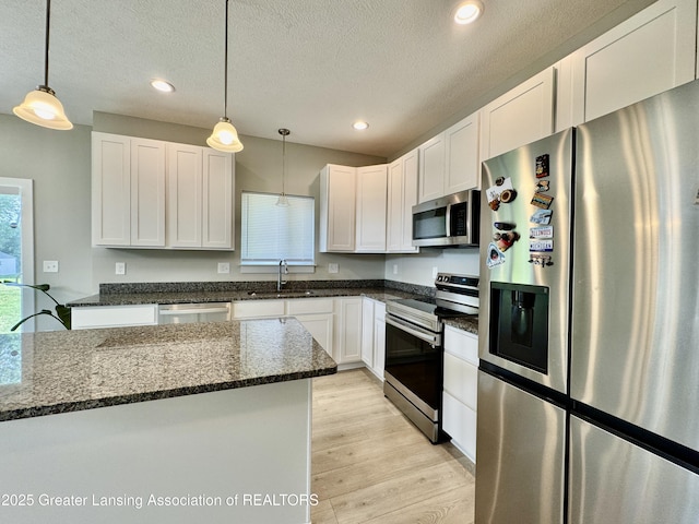 4314 Ringneck Ln, Holt, MI 48842 - kitchen with stainless steel appliances, light wood-style flooring, white cabinets, dark stone counters, and decorative light fixtures