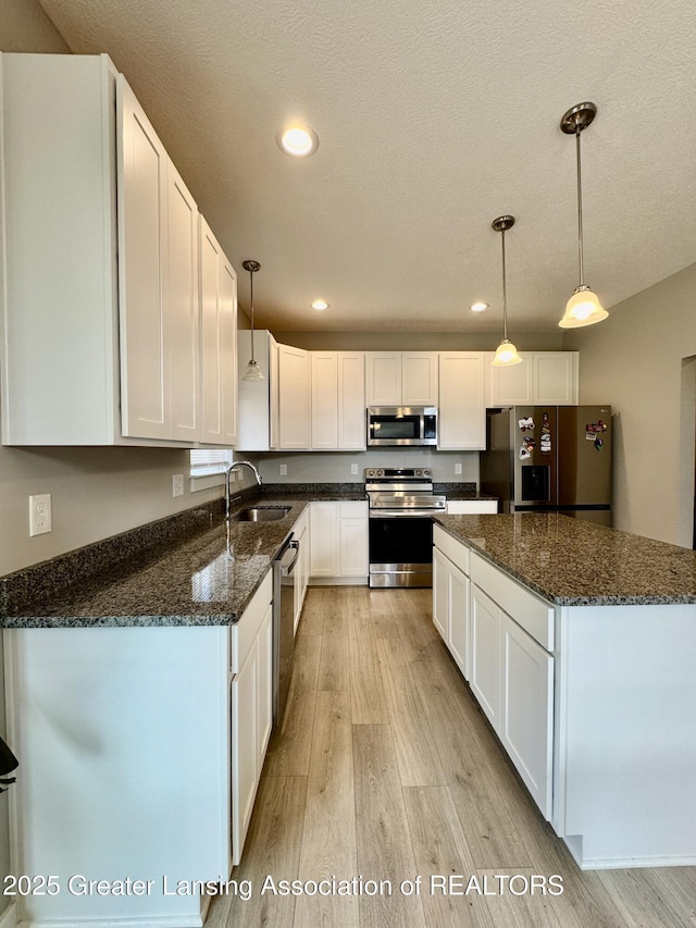 4314 Ringneck Ln, Holt, MI 48842 - kitchen with stainless steel appliances, light wood finished floors, white cabinetry, pendant lighting, and dark stone counters
