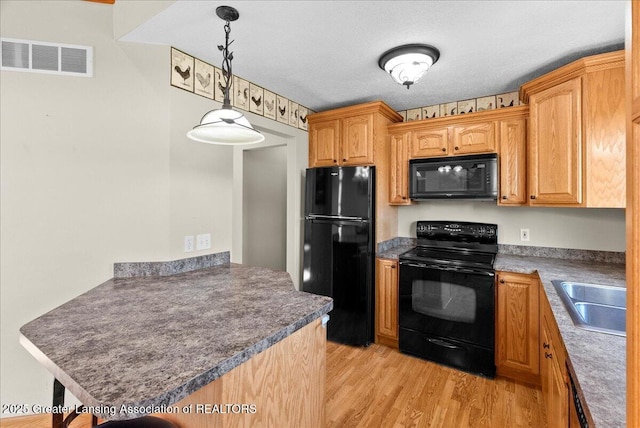 5159 E Pratt Rd, Saint Johns, MI 48879 - kitchen featuring black appliances, light wood-type flooring, a peninsula, pendant lighting, and dark countertops