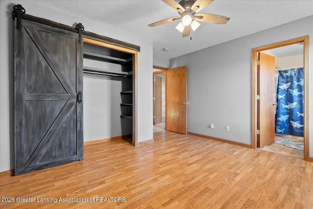 5159 E Pratt Rd, Saint Johns, MI 48879 - unfurnished bedroom featuring a barn door, light wood finished floors, a closet, a textured ceiling, and ceiling fan