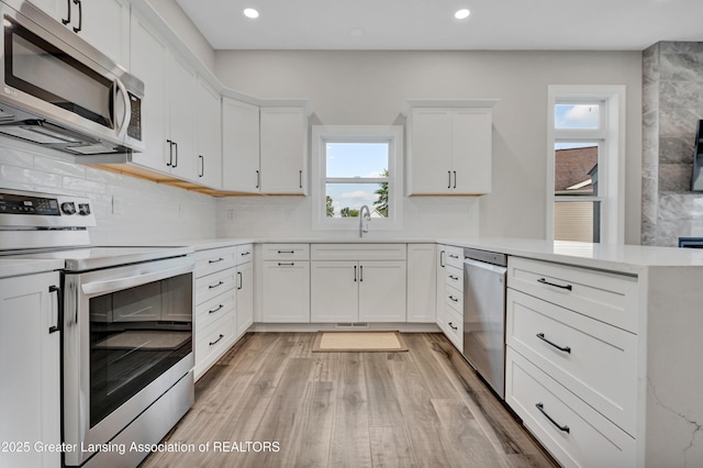 330 Vansickle Dr Unit 31, Charlotte, MI 48813 - kitchen with stainless steel appliances, a peninsula, light wood-style flooring, decorative backsplash, and white cabinetry