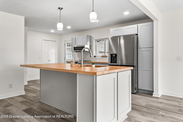1337 Shepard St, Crystal, MI 48818 - kitchen with butcher block counters, appliances with stainless steel finishes, a kitchen island with sink, light wood-style floors, and pendant lighting