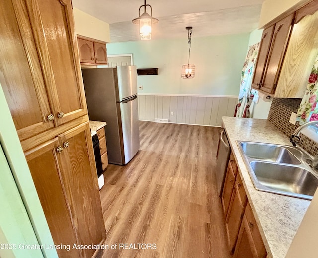 1214 Otto Rd Unit R1, Charlotte, MI 48813 - kitchen featuring appliances with stainless steel finishes, brown cabinets, light wood-type flooring, a wainscoted wall, and decorative light fixtures